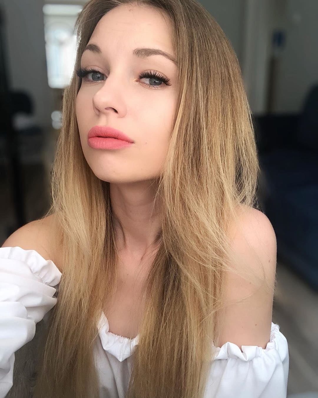 Blonde in white ruffled off-shoulder blouse, close-up portrait in soft indoor light.